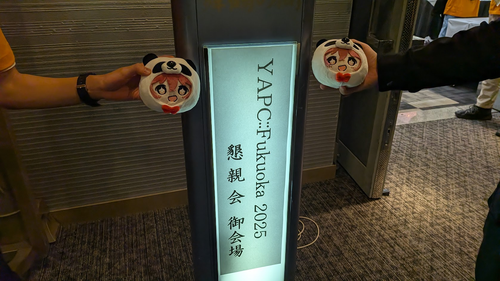 YAPC::Fukuoka 2025 懇親会御会場と書かれた看板を挟んでパンダ果穂ぬいをが写っている。
